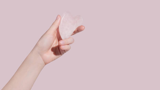 istock A female hand holding gua sha face massager on pink background. 1424313774