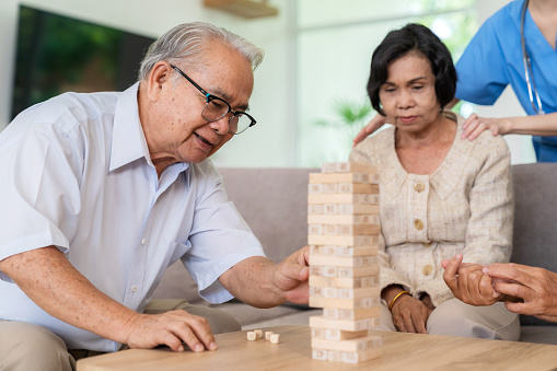 Dementia therapy in playful way. Group of senior elder people stay at nursing home, enjoy activity relation playing Jenga or tumbling tower wood block game. Training fingers and fine skills