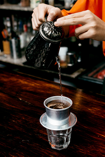 Traditional Vietnamese coffee is made from Robusta beans, which have a strong, bitter taste. Making Vietnamese coffee. Pouring hot water from goose neck kettle into glass through filter on dark background