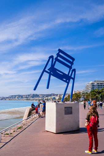 Tourist admiring the sculpture 'La Chaise de Sab', a work by the French artist Sabine Geraudie, installed in 2014 on the Promenade des Anglais, a very popular promenade along the Mediterranean coast of Nice.