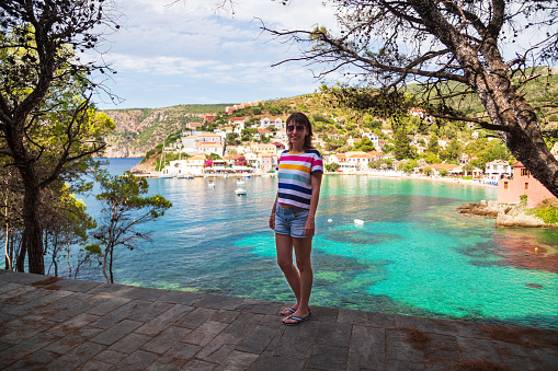 Young smiling woman in striped multicolored shirt and jeans shorts in green park at Asos village summer time. Extremely popular travel destination in Cephalonia, Greece, Europe