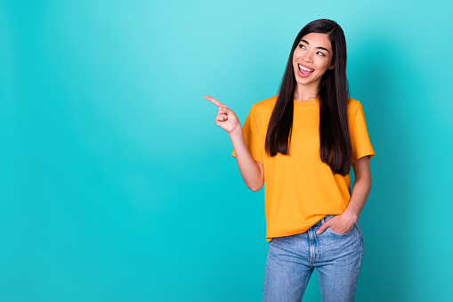 Photo of nice girlish adorable woman with long hairstyle wear yellow t-short directing empty space isolated on turquoise color background.