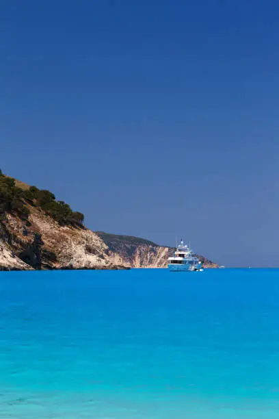 Photo of White yacht anchored in fantastic Myrtos Beach turquoise and blue bay. Summer scenery of famous and extremely popular travel destination in Cephalonia island, Greece, Europe