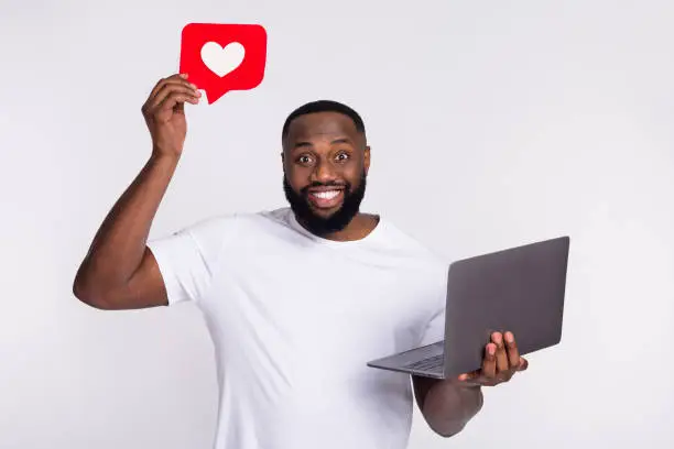 Photo of Photo of funky charming man wear casual t-shirt holding heart sign typing modern device isolated white color background