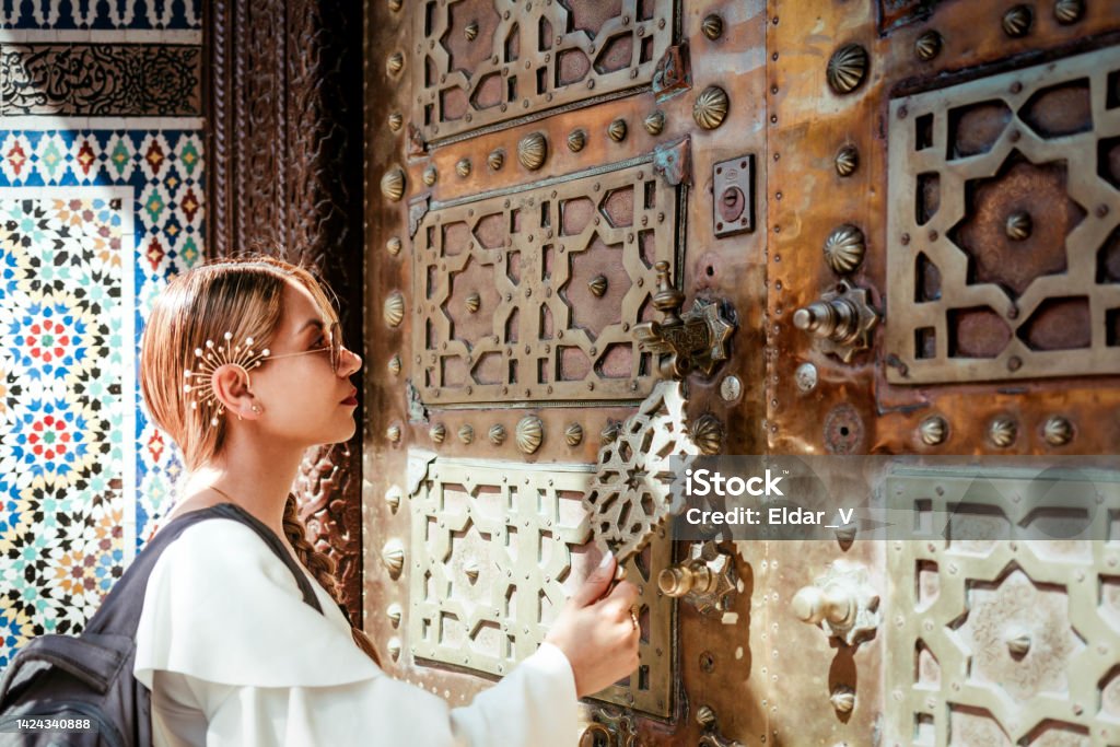 woman knocking on a sacred door Latin woman knocking on a sacred door, wears a white blouse, sunglasses and a traveling briefcase, the door has decorations in wood and gold. Church Stock Photo