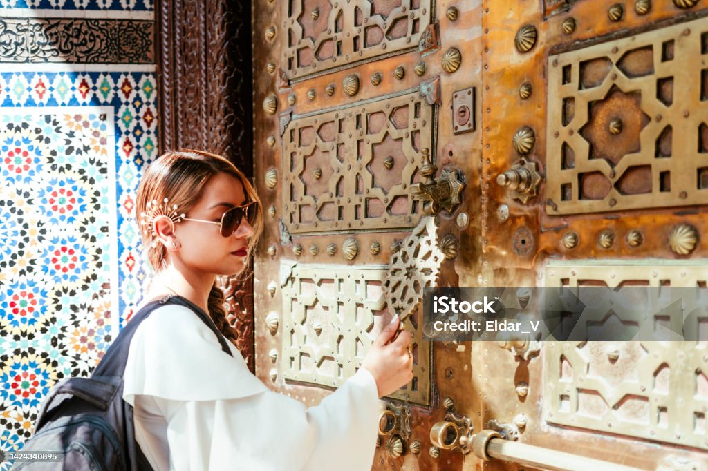 woman knocking on a Moroccan door young woman knocking on a door, to enter a sacred temple, to meditate, door with a lot of ornamentation. Adult Stock Photo