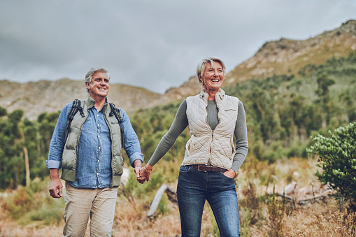Senior happy couple holding hands and smile while out hiking in nature, mountain or hill together. Elderly man and woman smiling during a hike looking happy in nature enjoy retirement and love