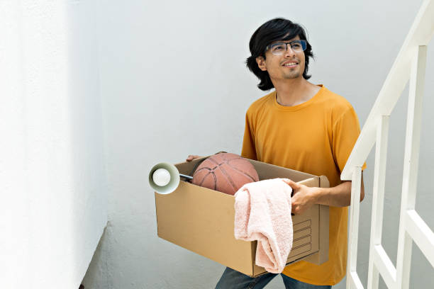 istock young man holding a moving box, climbing up stairs inside a building 1424352286
