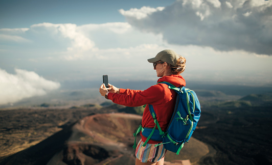 Woman hiker taking photo with smart phone  on volcano crater.
