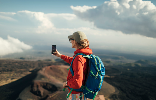 Woman hiker taking photo with smart phone  on volcano crater.