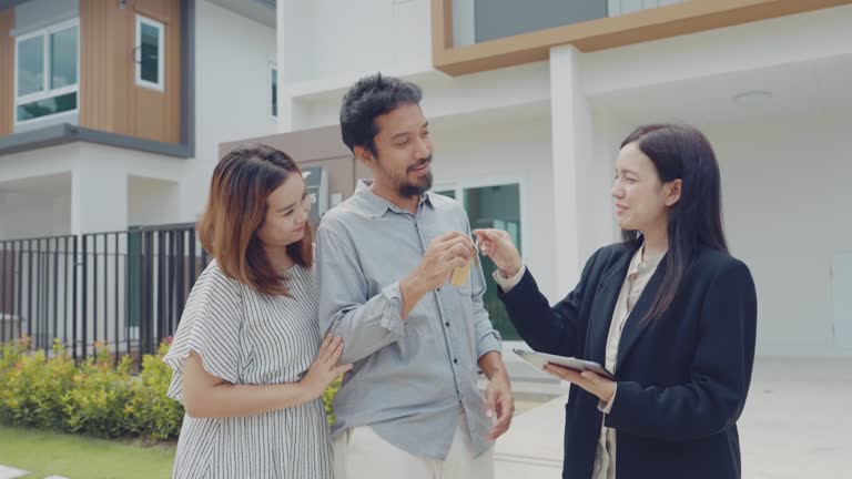 Asian couple looking happy in front of their new house.