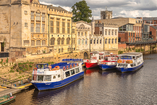 York, UK.  September 7, 2022.  A medieval civic building stands beside a river. There are tour boats moored alongside and a cloudy sky is above.
