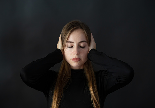 Blond woman with closed eyes covering her ears with her hands.
She is from Russia.
Indoor Photoshoot.