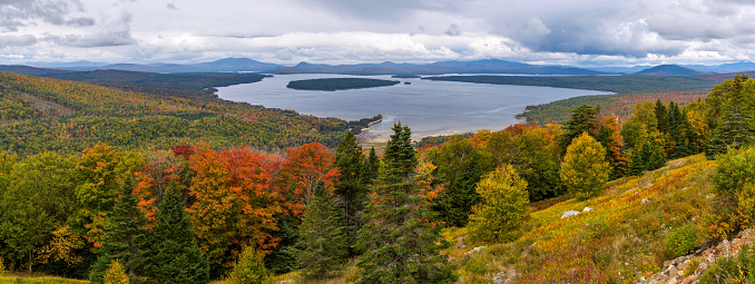 A panoramic overview of Mooselookmeguntic Lake and its surrounding rolling hills on a colorful but stormy Autumn day, as seen from Height of Land at side of Route 17, Rangeley Lakes National Scenic Byway. Western Maine, USA.