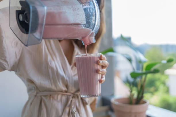 young woman pours a breakfast smoothie into a glass - transparent holding glass focus on foreground imagens e fotografias de stock