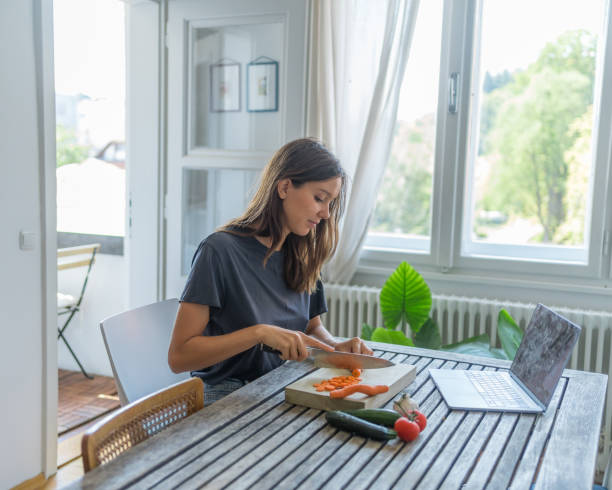 istock Young woman uses computer for recipe and makes meal 1424371383