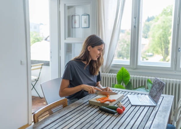 istock Young woman uses computer for recipe and makes meal 1424371409