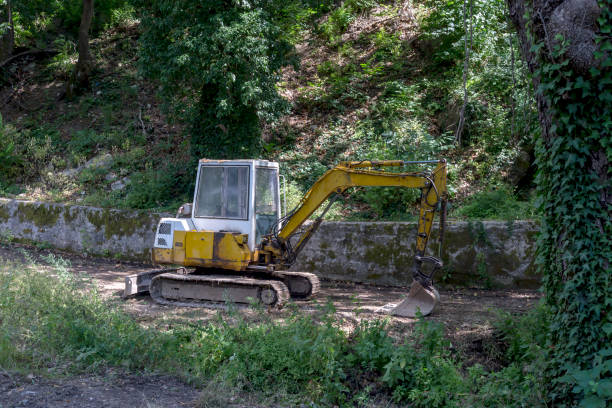 Excavator single-bucket  for for earthworks in the mountains, is parked on a path in a forest area on a summer day