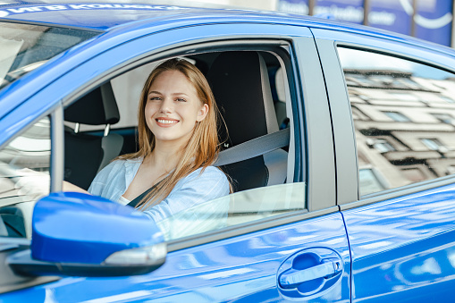 Young and cheerful woman sitting in the car and looking at the camera