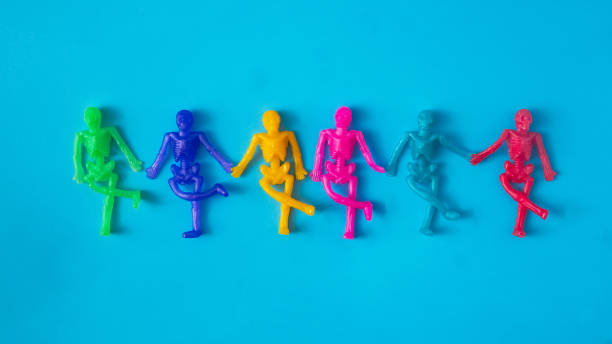 istock Mini skeletons in different colors holding hands on blue background.  Surreal spooky creative concept for Halloween celebration banner or party invitation 1424374045