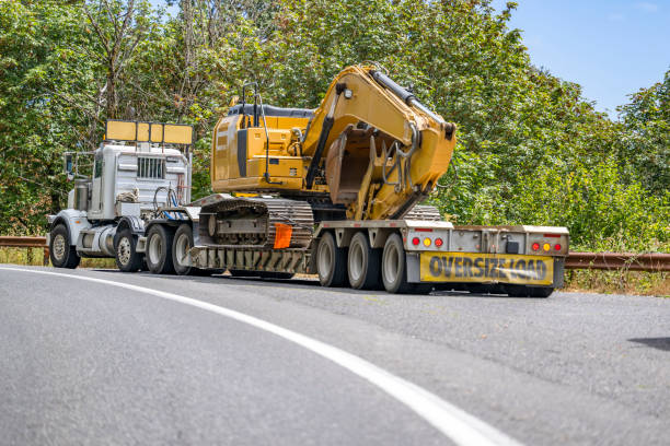 istock Powerful big rig semi truck with oversize signs on the cab and step down semi trailer transporting excavator climbing uphill on the turning narrow road 1424377347