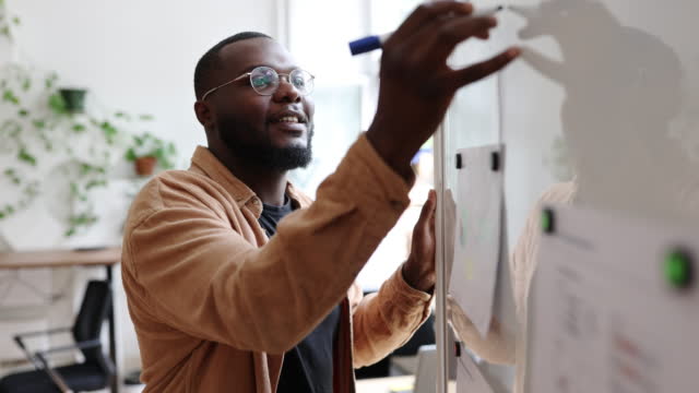 African man writing on a whiteboard and smiling at startup office