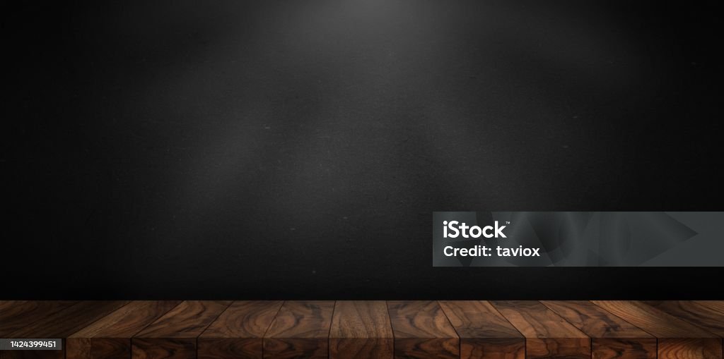 Wooden table made with natural wood planks with a concrete block wall background in a dark room, rustic environment to display artisan elements, meats or Mediterranean products. Black Background Stock Photo