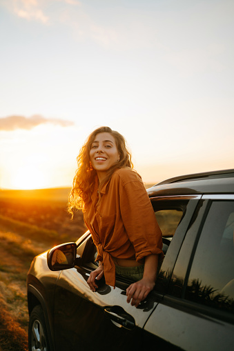 Young woman is resting and enjoying sunset in the car. Lifestyle, travel, tourism, nature, active life.