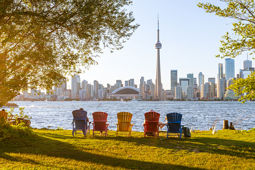 Colorful adirondack chairs on Toronto Island Park at sunset time. Toronto City downtown skyline in the background. Ontario, Canada.
