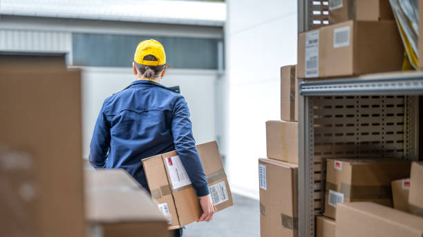 istock Warehouse worker walking with cardboard box, unloading truck, back view 1424425553