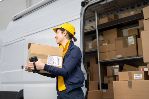 istock Female courier carrying carboard box, unloading delivery truck 1424425566