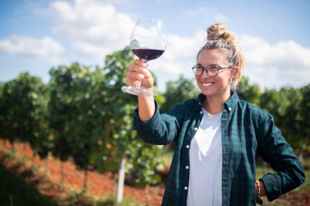 женщина смотрит на бокал с вином, стоящий на открытом воздухе на винограднике - red grape grape fruit sweet food стоковые фото и изображения