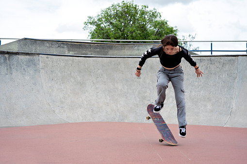 Young latina millennial girl performing tricks on a skateboard in a skatepark in urban city environment. Lifestyle and tricks on a skateboard.