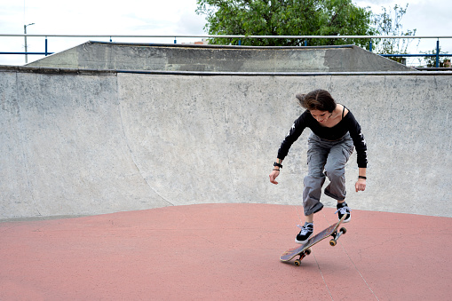 Young latina millennial girl performing tricks on a skateboard in a skatepark in urban city environment. Lifestyle and tricks on a skateboard.