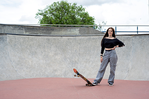 Portrait of a young latina skateboarder looking at the camera with a skateboard in a skatepark in the urban environment of the city of bogotá. Lifestyle and skate tricks.