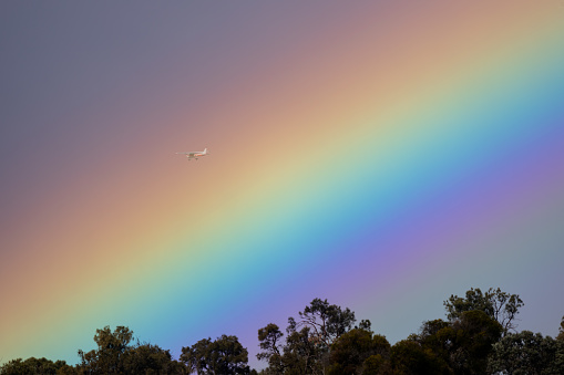 A plane is flying across a beautiful big rainbow in country side of Australia