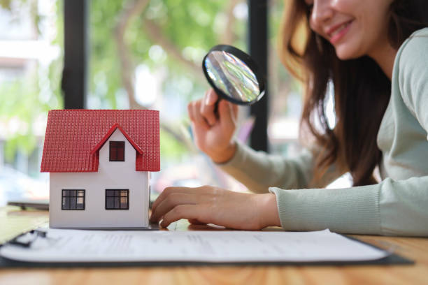 woman looking at the house model with a magnifying glass. real estate appraisal, land valuation and house selection concept. - find home insurance stockfoto