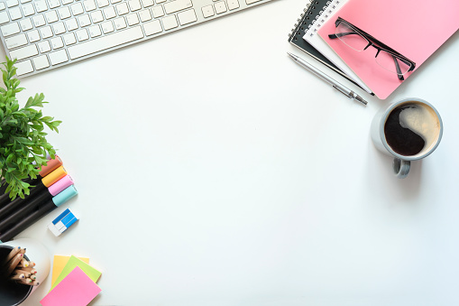 White office desk with notepad, sticky notes, glasses and coffee cup. Top view with copy space.