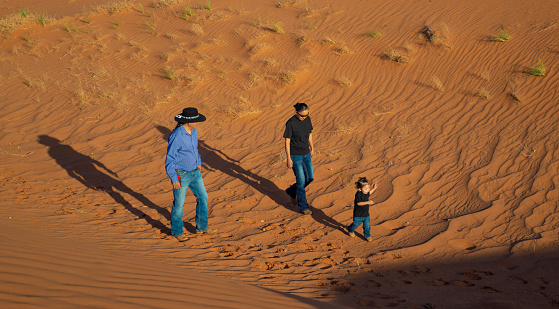 Navajo man and his Family walking on the sand dunes in Monument Valley at sunset