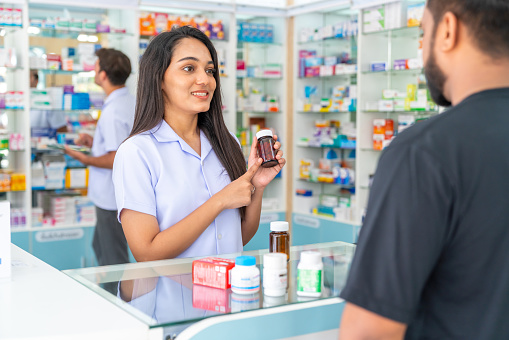 Professional Indian woman pharmacist medication recommendation about medicine, drugs and supplements to male patient customer in modern drugstore. Medical pharmacy and healthcare providers concept.