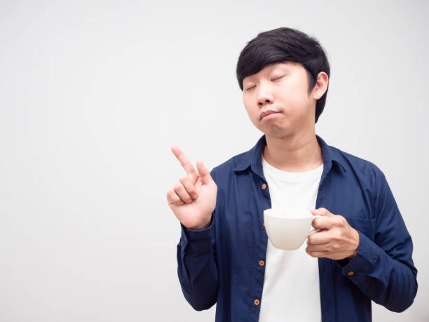 istock Sleepy man holding coffee cup close eyes and point finger at copy space white background 1424479843