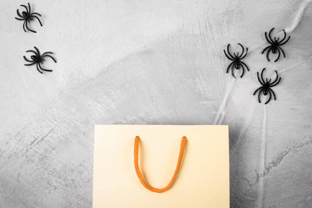 istock Festive Halloween background with copy space. Mockup with an empty shopping bag on a gray gloomy background with decorations and gifts top view, flat lay. 1424498175