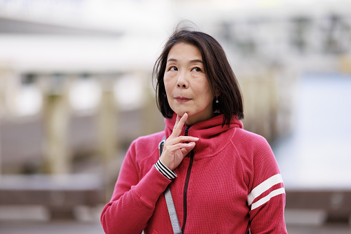 Asian woman standing outdoors, deep in thought.
