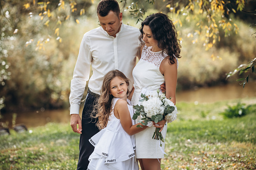 Family mother, father and daughter are beautiful and happy together on a holiday, in white clothes and with a bouquet, in nature