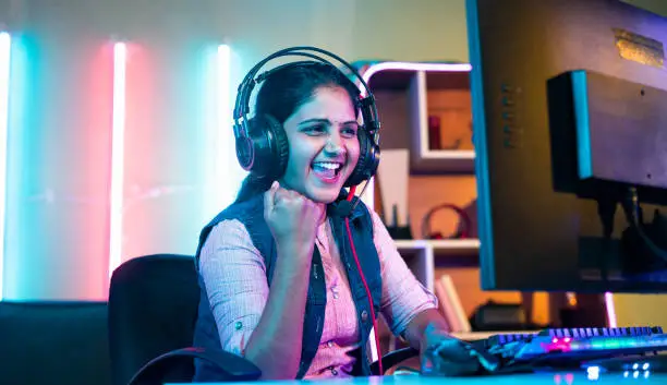 Photo of happy gamer celebrating win or victory while playing online video game tournament on computer at home - concept of success, championship and live streaming.