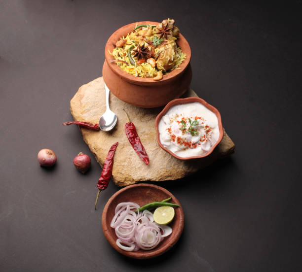 chicken dum biriyani served in copper handi or bowl with onion raita.