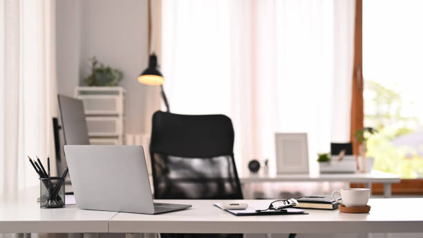 Horizontal image of laptop computer, documents and various office supplies on white table in modern interior. stock photo