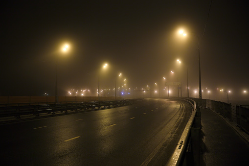 wet road with lights at night in the fog. there is blue lights in the distance.