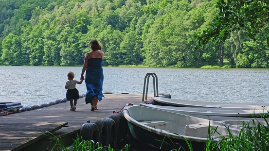 Mother and Child Toddler Walking Along Wooden Quay at Lake Harbor for Row Boats