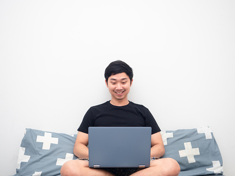 Asian man sit on the bed and using laptop for working white background